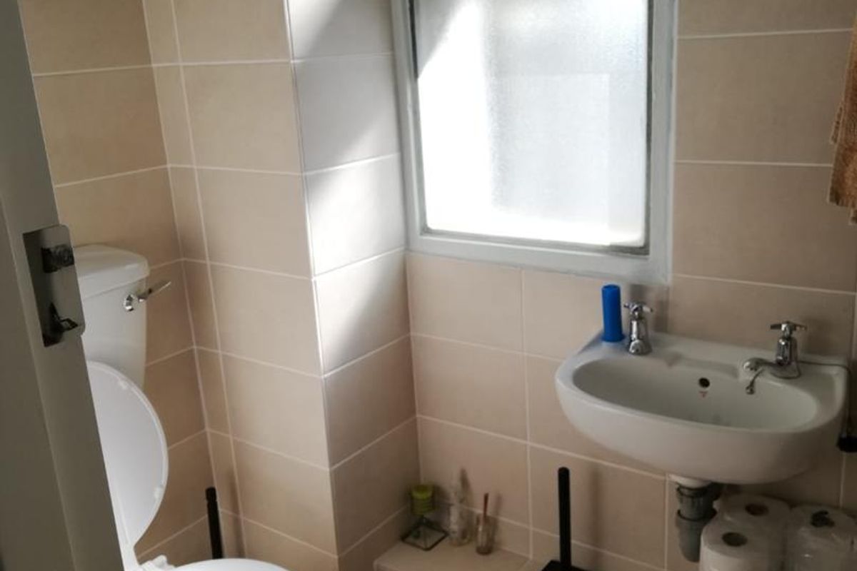 A compact bathroom featuring a wall-mounted basin, toilet, and neutral tiled finishes with a window for natural light.