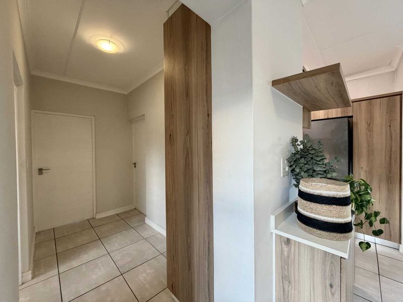 A clean, well-maintained hallway featuring neutral tiled flooring and modern wood-finish built-in cabinetry, providing a bright and functional transition space.