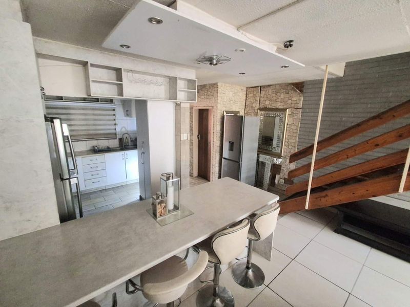 Open plan kitchen and living area featuring a breakfast bar, tiled flooring, stone accent wall, and a wooden staircase.