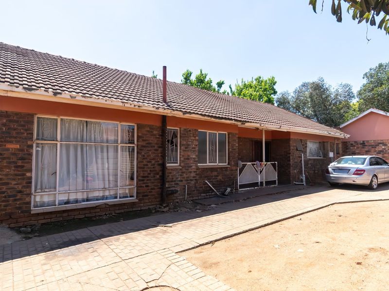 Front elevation of a single-story brick house featuring a tiled roof, paved driveway, and security window bars.
