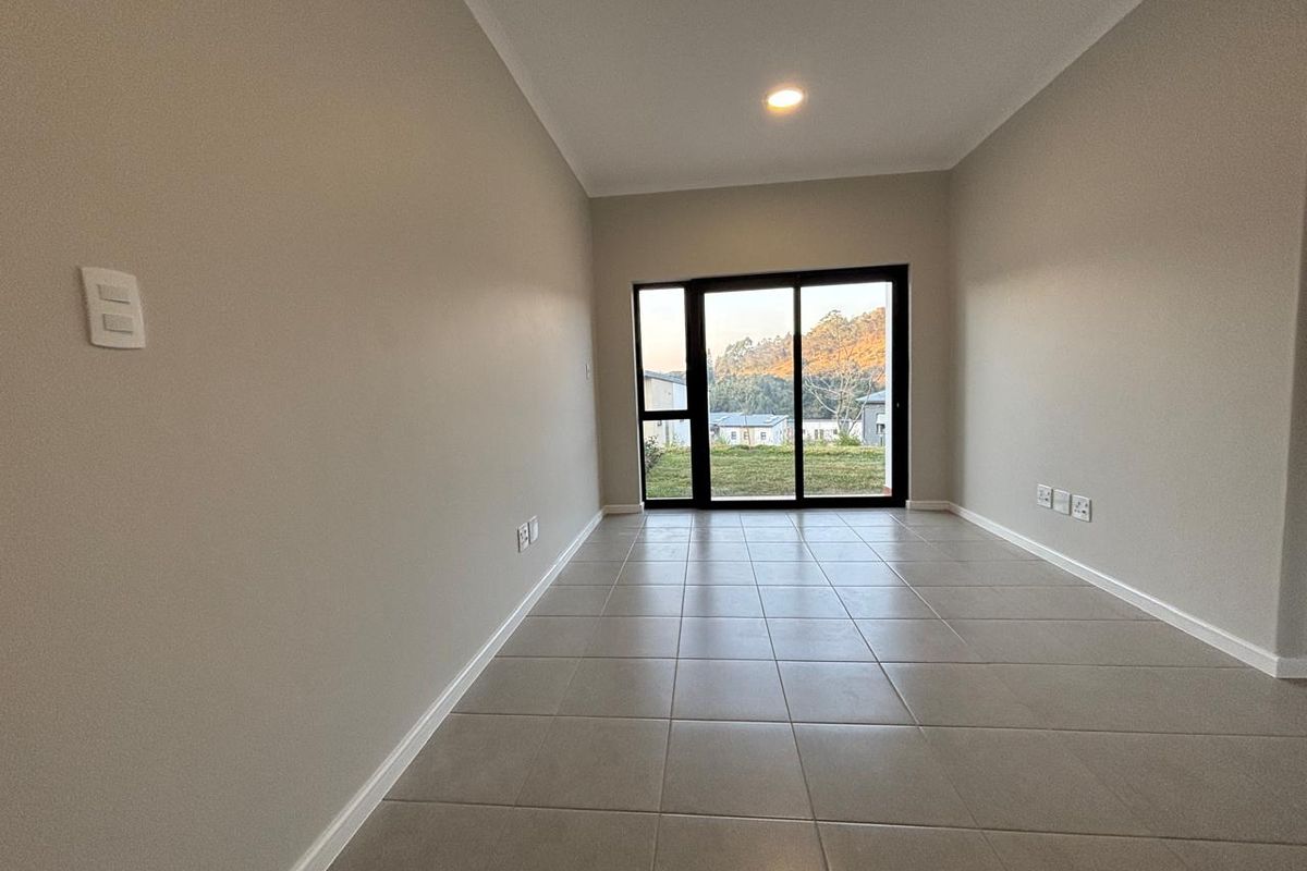 A bright, empty living area featuring neutral tiled flooring, recessed lighting, and a sliding glass door providing access to the exterior.