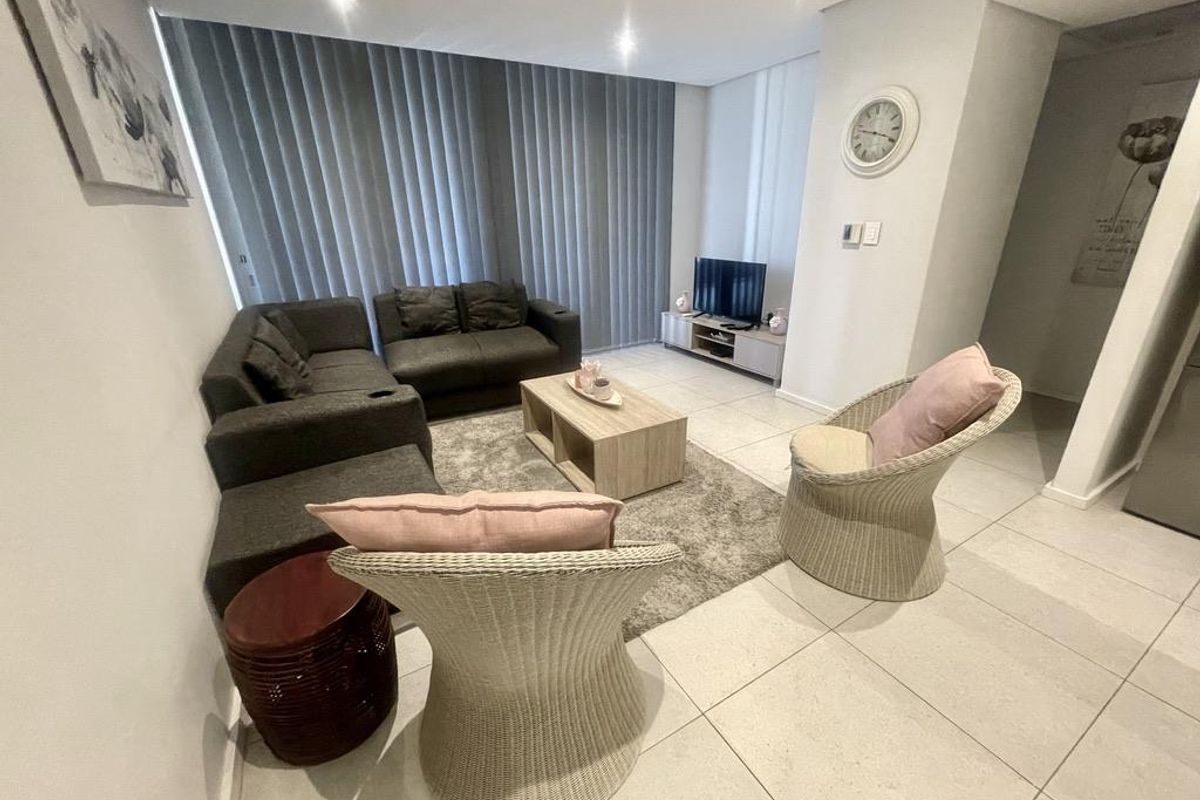 A bright and modern living room featuring large format floor tiles, recessed downlighting, and floor-to-ceiling window treatments.