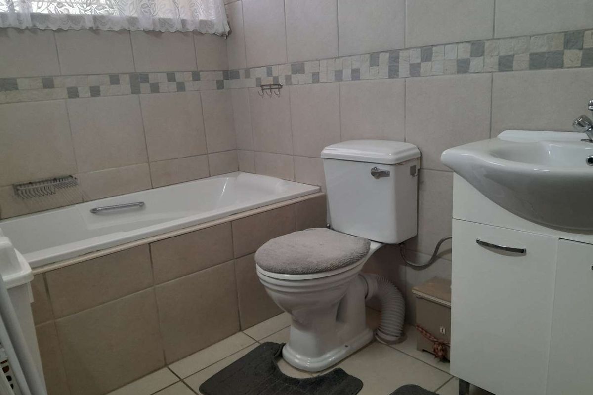 A functional bathroom featuring a built-in bathtub, a standard toilet, and a vanity basin with storage cabinetry.