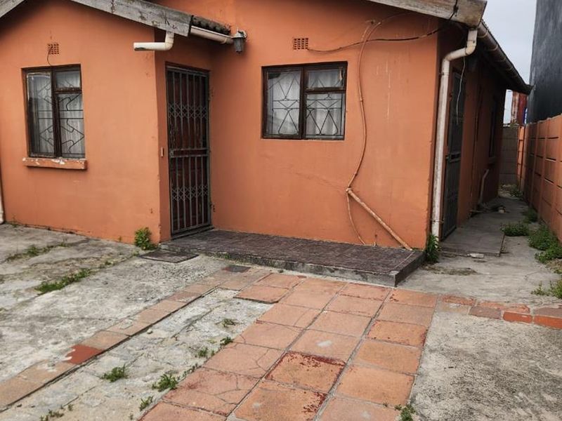 Front view of a detached house featuring a tiled walkway, security gates, and weathered exterior walls requiring maintenance and cosmetic updates.