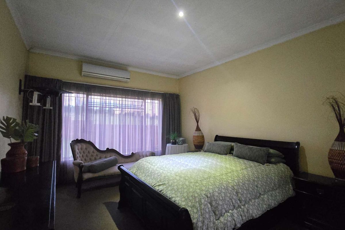 A spacious bedroom featuring a wall-mounted split-system air conditioner, cove cornicing, and a large window with integrated curtain tracks.