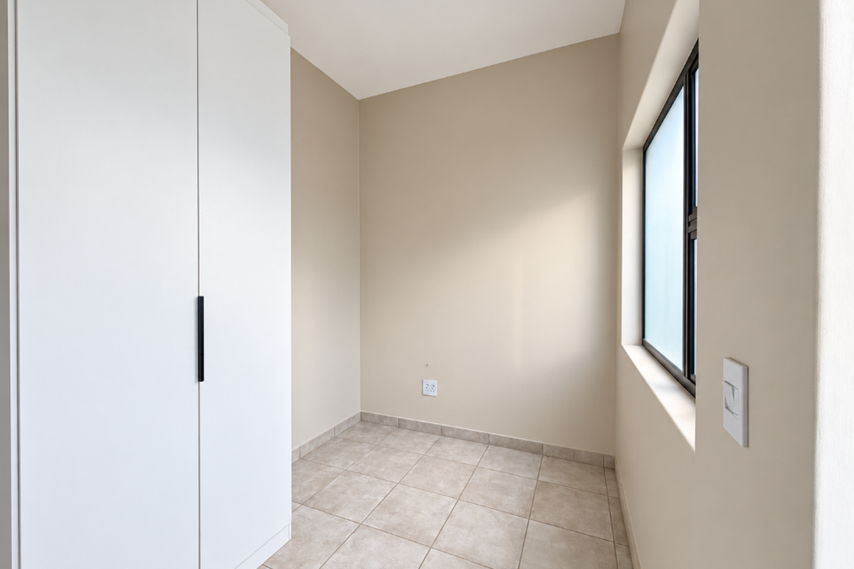 A clean, empty bedroom featuring neutral tiled flooring, a modern built-in wardrobe, and a large window providing natural light.