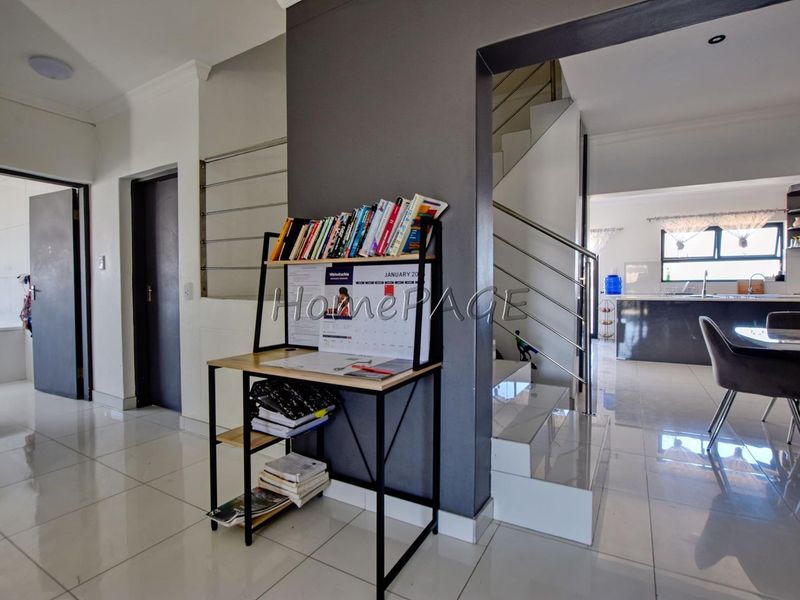 Open plan living area featuring tiled floors, a modern staircase with stainless steel balustrades, and a view into the kitchen space.