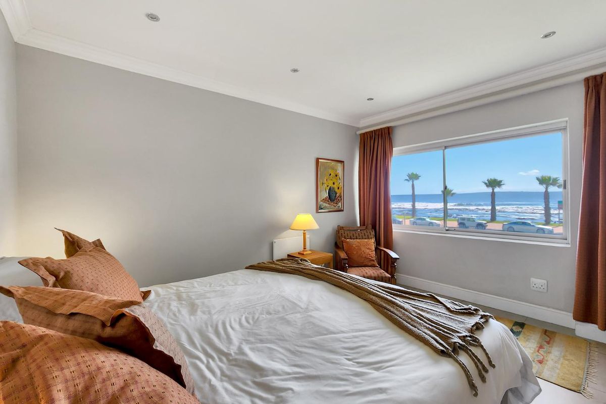 A bright bedroom featuring neutral walls, recessed lighting, and a large sliding window offering scenic ocean views.