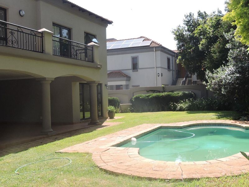 Rear view of the property featuring a covered patio, upper balcony with wrought iron railings, and a swimming pool set in a landscaped garden.