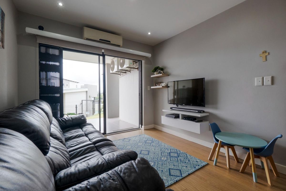 A modern living room featuring wood-look flooring, recessed ceiling lighting, a wall-mounted media console, and sliding glass doors leading to a private balcony.