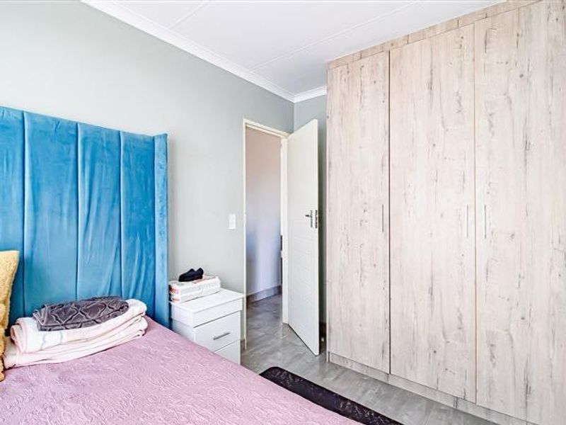 A well-maintained bedroom featuring light wood-finish built-in wardrobes, neutral wall tones, and tiled flooring.