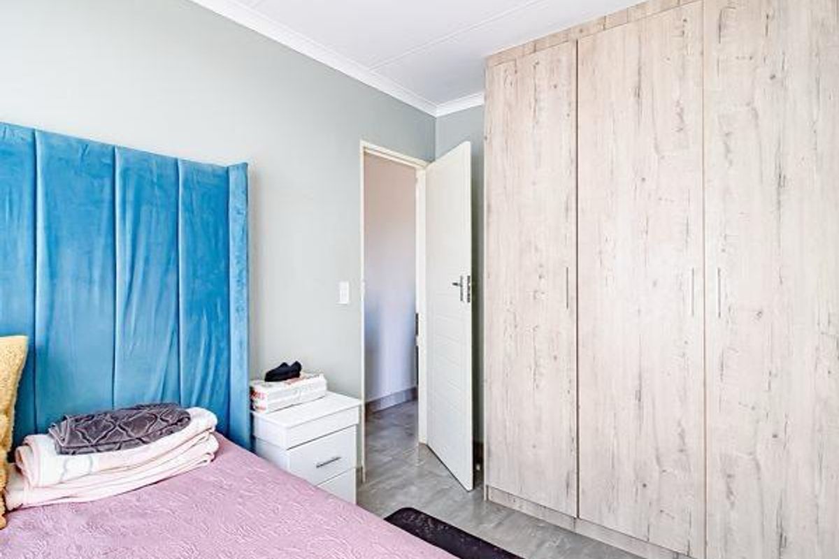 A well-maintained bedroom featuring light wood-finish built-in wardrobes, neutral wall tones, and tiled flooring.