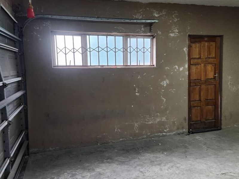 An empty garage space featuring a sectional door, security-barred window, and a timber door, requiring cosmetic updates to the walls and flooring.