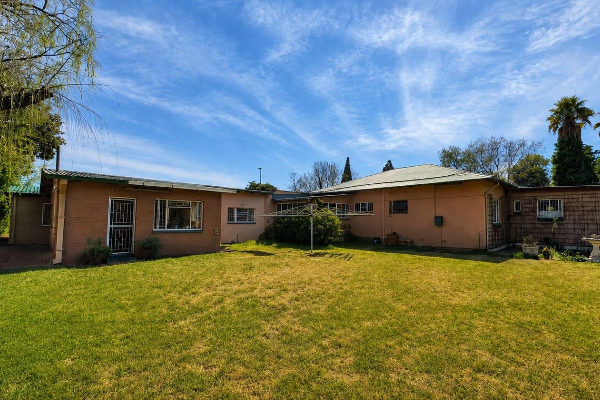 Rear view of the house featuring a brick and rendered facade, metal roofing, and a spacious backyard with a rotary clothesline.