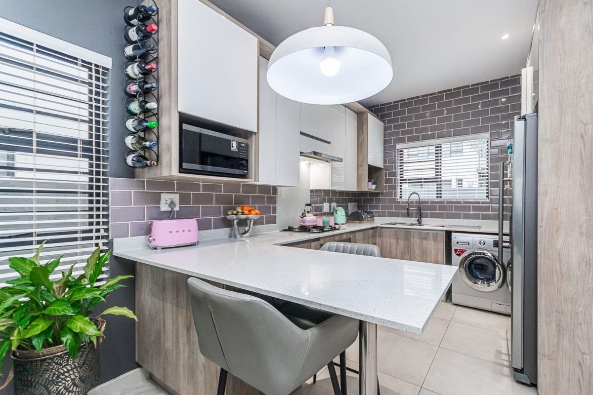 Modern kitchen featuring stone countertops, subway tile backsplash, built-in microwave, integrated hob, and dedicated space for a washing machine.