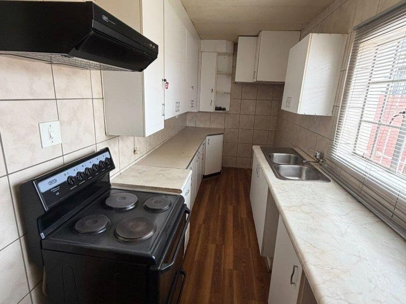 A functional galley-style kitchen featuring laminate countertops, a double stainless steel sink, electric stove, extractor fan, and ample wall-mounted cabinetry.