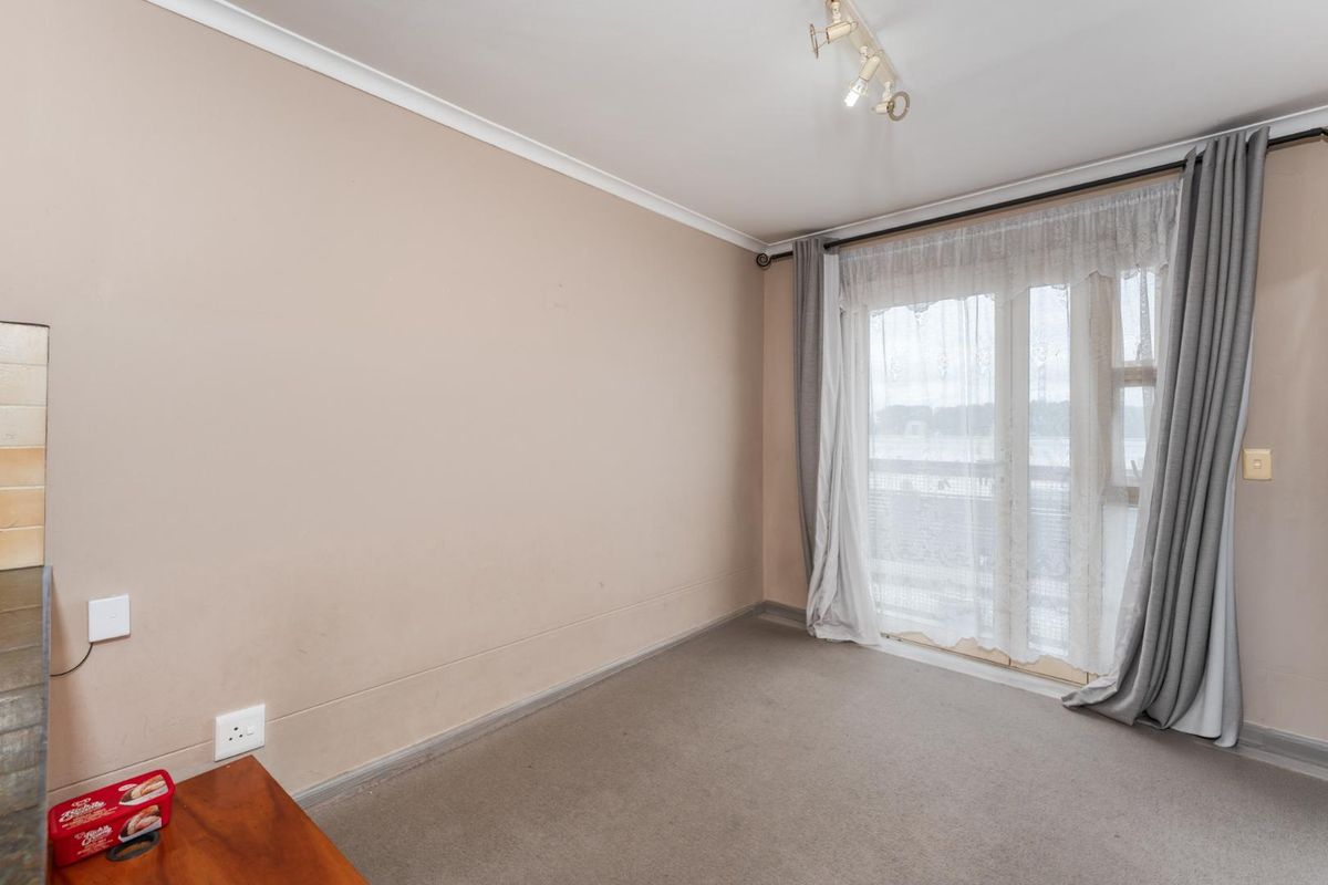 A bright, empty bedroom featuring neutral walls, carpeted flooring, and a sliding glass door providing access to an outdoor area.