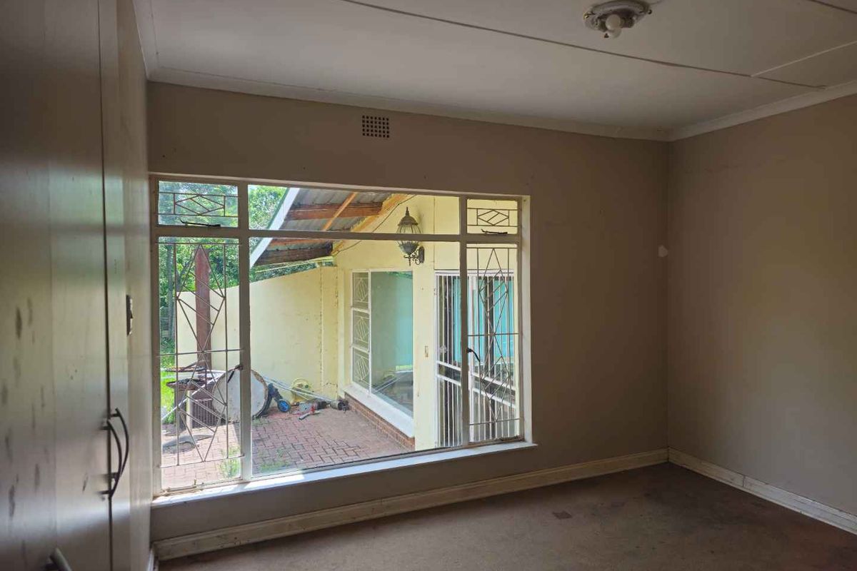 A vacant bedroom featuring built-in cupboards, large windows with security bars, and direct views of the rear patio area.