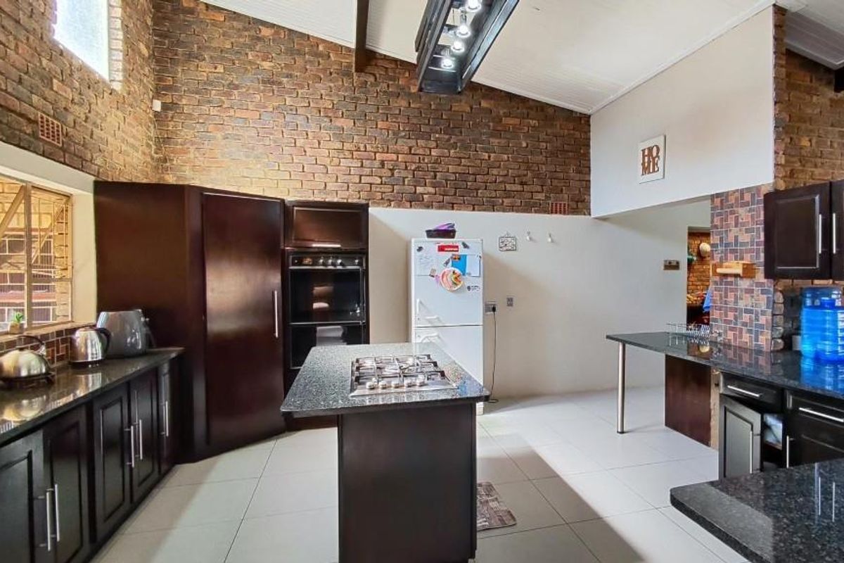 Spacious kitchen featuring dark cabinetry, granite countertops, a central island with a built-in gas hob, and exposed brick feature walls with high ceilings.