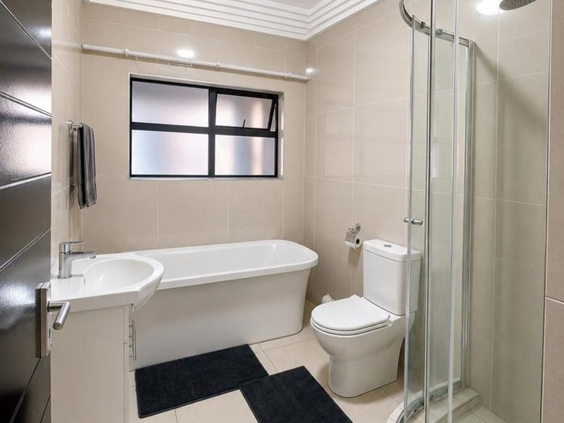 Modern bathroom featuring a freestanding bathtub, a separate curved glass shower enclosure, a vanity basin, and neutral floor-to-ceiling tiling.