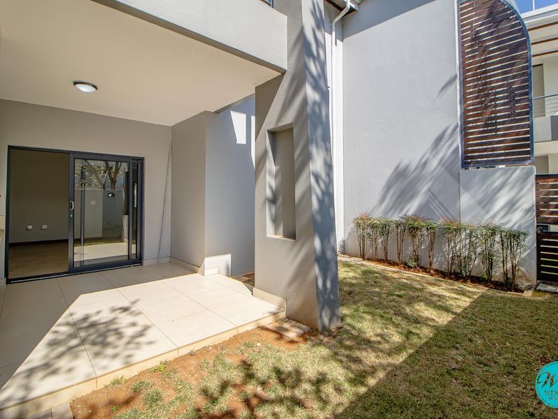 A covered patio area featuring tiled flooring, a built-in braai, and direct access to the garden through a sliding glass door.