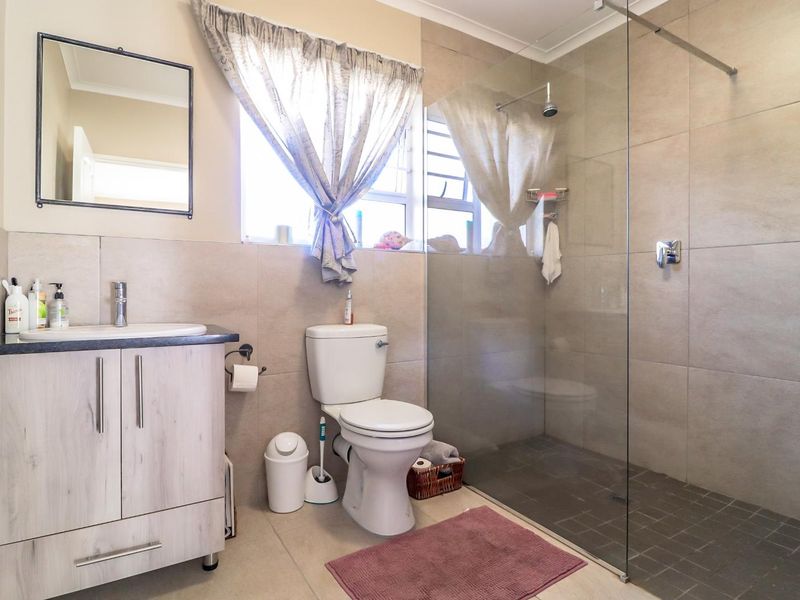 Modern bathroom featuring a walk-in shower with glass screen, vanity cabinet with basin, and neutral wall and floor tiling.