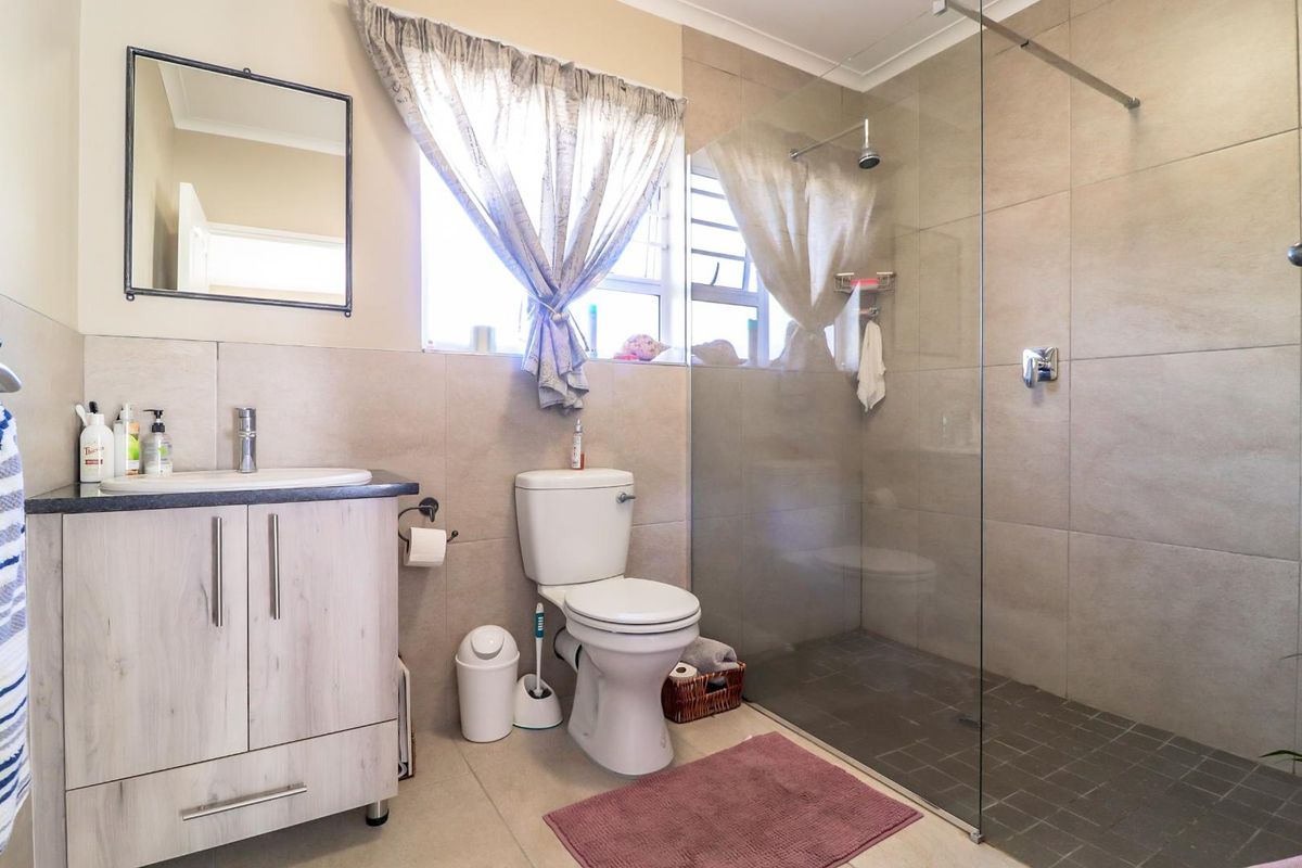 Modern bathroom featuring a walk-in shower with glass screen, vanity cabinet with basin, and neutral wall and floor tiling.