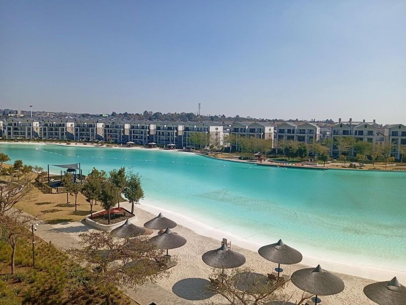 Elevated view overlooking a large turquoise artificial lagoon with a sandy beach and surrounding residential apartment complex.