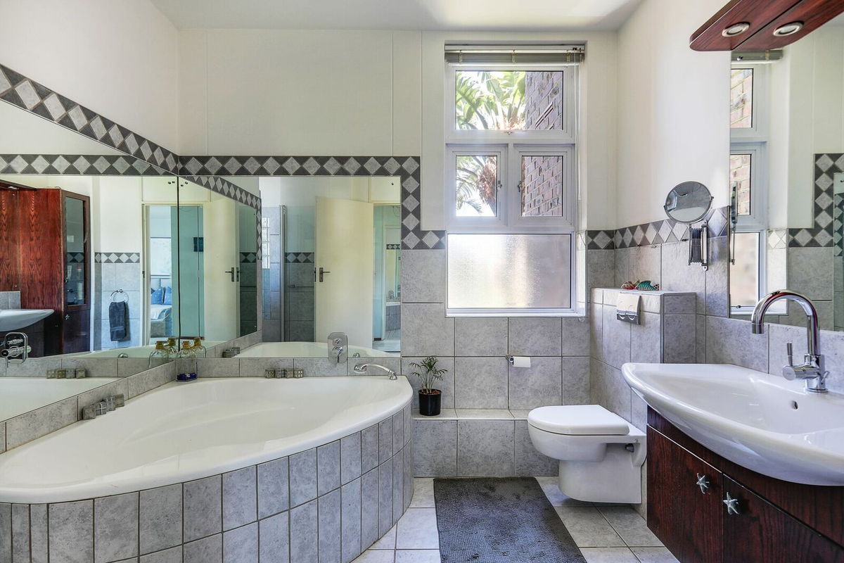 A functional bathroom featuring a corner bathtub, wall-mounted toilet, vanity cabinet with basin, and large wall mirrors, providing a practical layout.