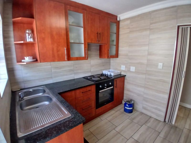 A functional kitchen featuring warm-toned wooden cabinetry, granite countertops, a built-in oven, electric hob, and neutral tiled finishes throughout.