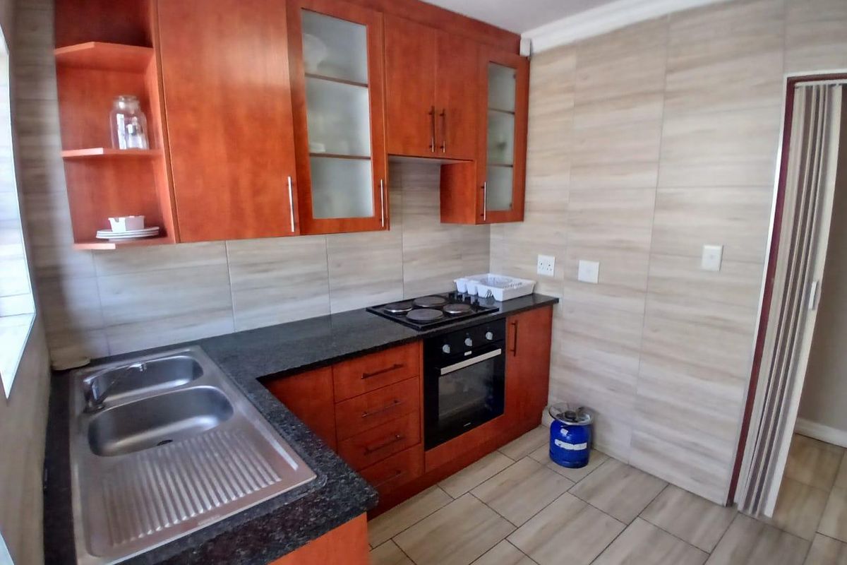 A functional kitchen featuring warm-toned wooden cabinetry, granite countertops, a built-in oven, electric hob, and neutral tiled finishes throughout.