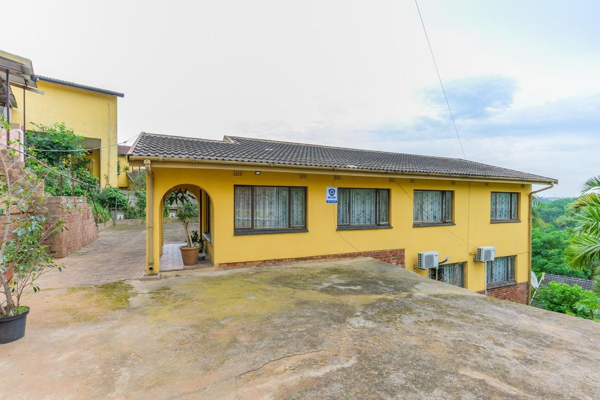 Rear exterior view of a yellow house featuring a concrete driveway, tiled roof, and wall-mounted air conditioning units.