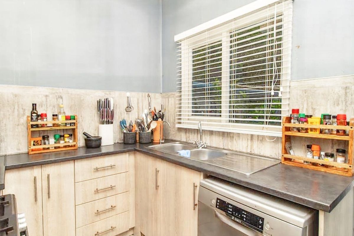 A functional kitchen featuring light wood-finish cabinetry, dark laminate countertops, a stainless steel double sink, and tiled splashbacks.