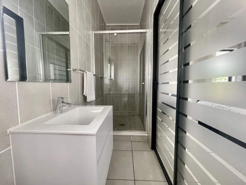 Modern bathroom featuring a sleek vanity with basin, a glass-enclosed shower, and neutral floor-to-ceiling wall tiling.