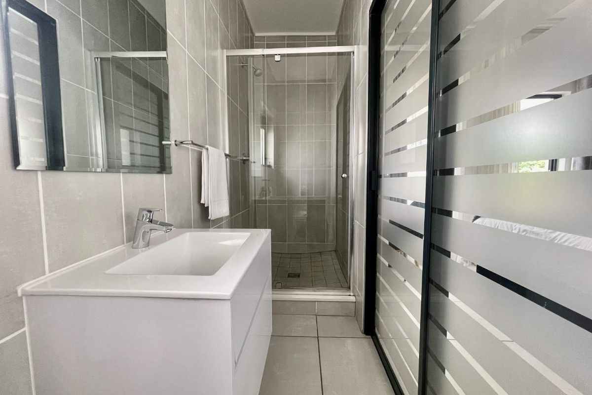 Modern bathroom featuring a sleek vanity with basin, a glass-enclosed shower, and neutral floor-to-ceiling wall tiling.