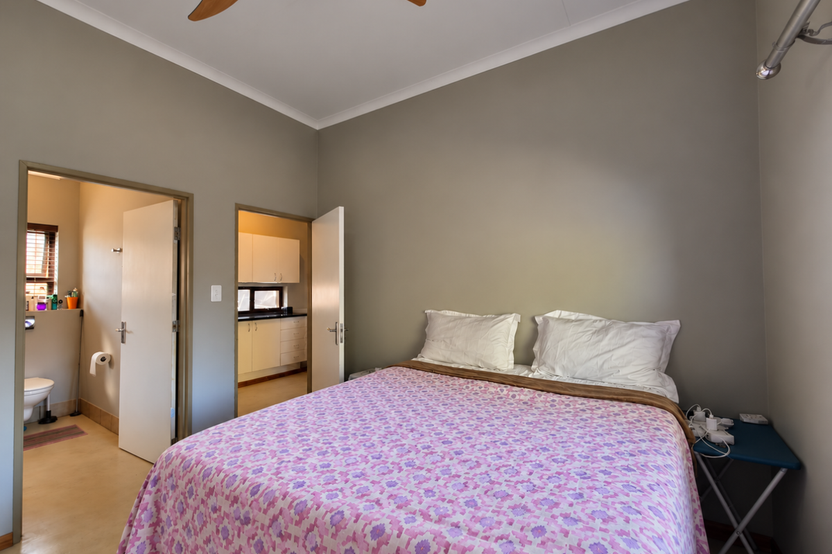 A bedroom featuring a ceiling fan and coving, with direct access to an en-suite bathroom and a glimpse of the kitchen area.