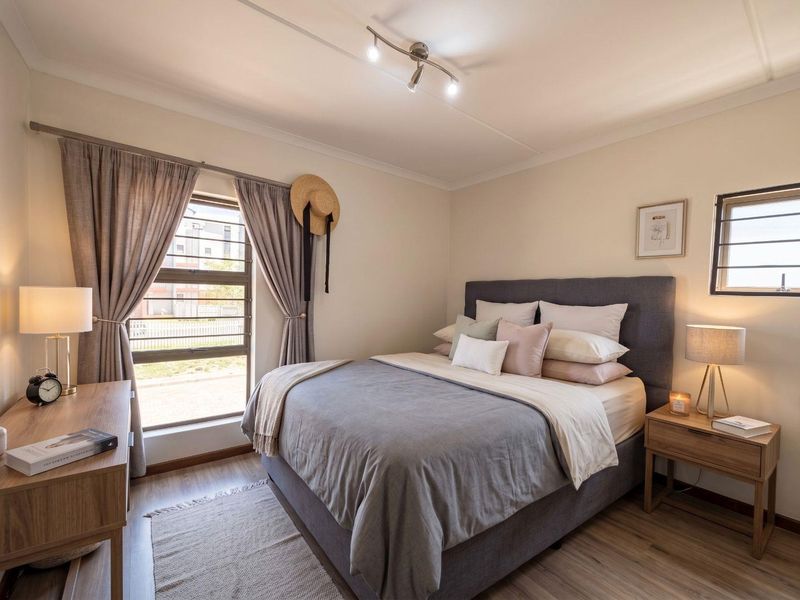 A well-maintained bedroom featuring laminate flooring, neutral walls, and a window fitted with security bars, providing a bright and comfortable living space.