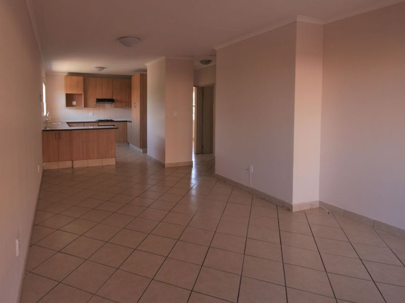 An open-plan living and kitchen area featuring neutral walls, ceramic tiled flooring, and functional built-in wooden cabinetry.