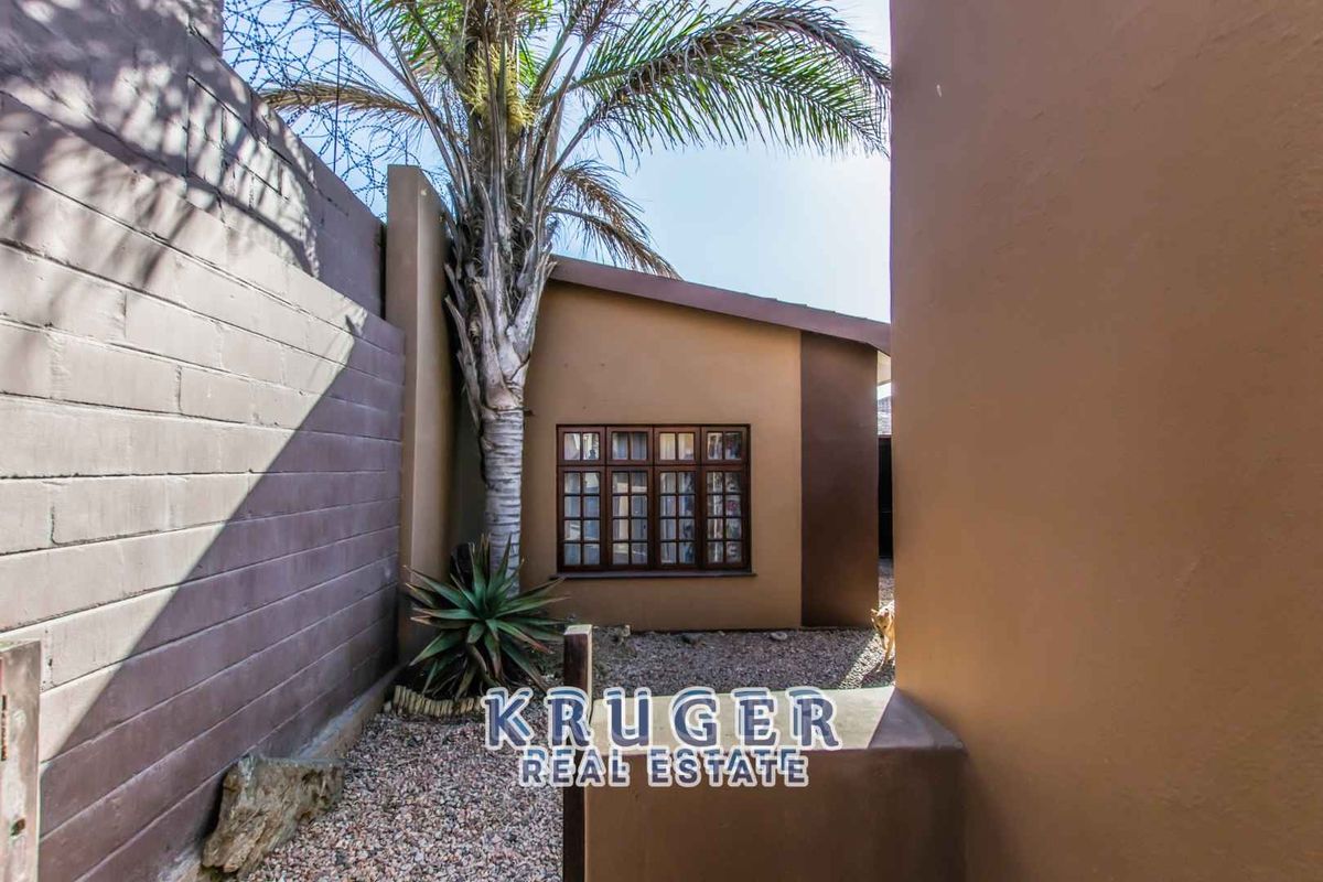 A private side courtyard area featuring a gravel surface, perimeter boundary walls, and a mature palm tree.