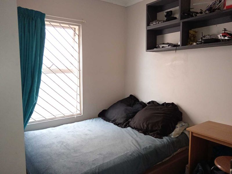 A compact bedroom featuring a window with security bars and built-in wall shelving.