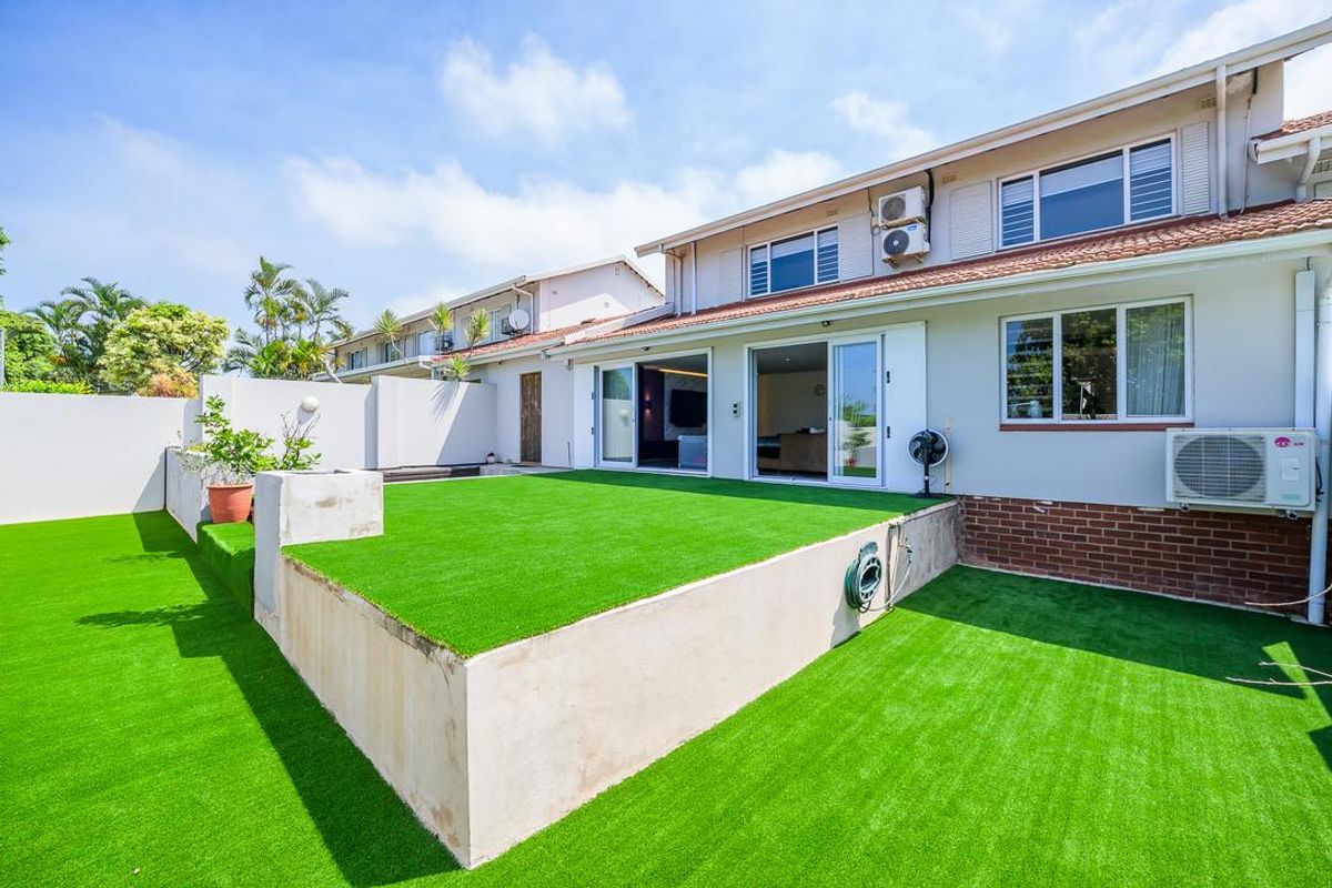 Rear view of the townhouse featuring a raised artificial lawn terrace, sliding glass doors, and a private garden area.
