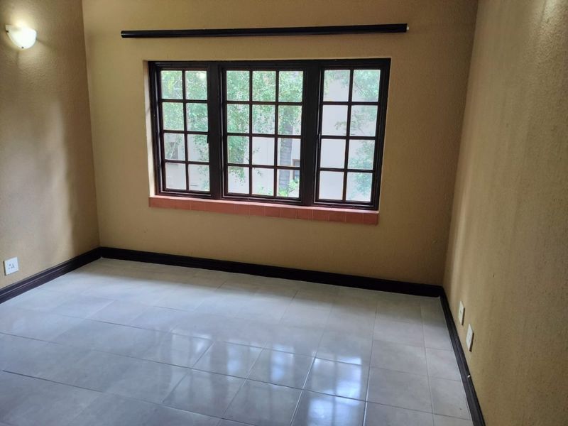 An empty bedroom featuring tiled flooring, a multi-pane window, and neutral wall tones, offering a blank canvas for personalization.