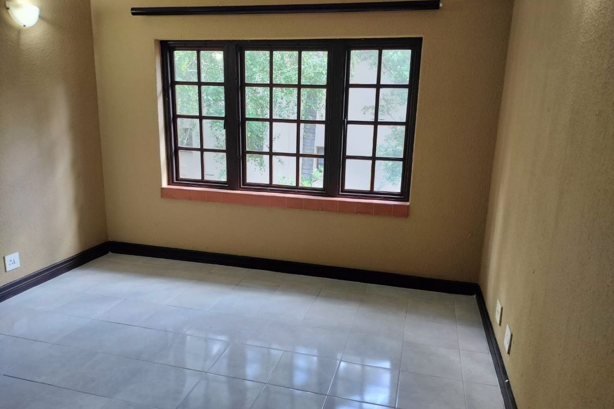An empty bedroom featuring tiled flooring, a multi-pane window, and neutral wall tones, offering a blank canvas for personalization.