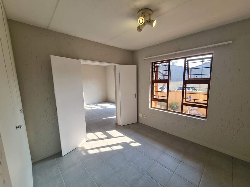 An empty bedroom featuring tiled flooring, built-in cupboard storage, and steel-framed windows, offering a neutral space ready for personalization.