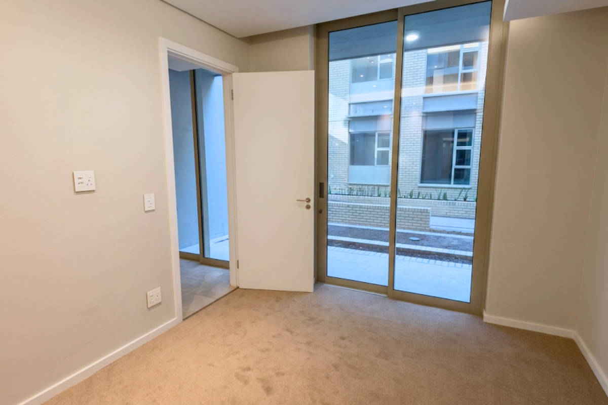 A bright, empty bedroom featuring neutral carpeting, a sliding glass door leading to an outdoor area, and a doorway connecting to an adjacent space.