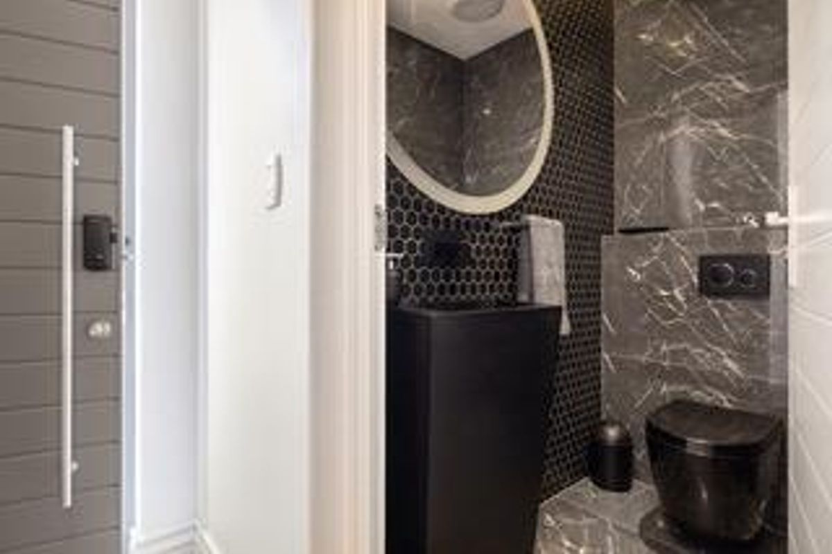 Modern guest bathroom featuring a sleek black pedestal basin, wall-mounted toilet, and stylish dark marble-effect tiling with a circular mirror.