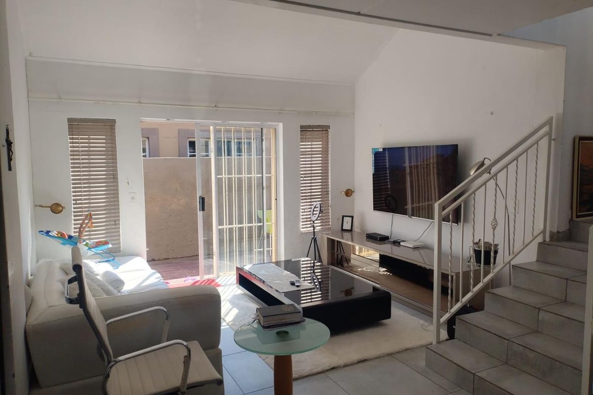 Bright living room featuring tiled floors, a vaulted ceiling, and a sliding glass door providing access to the outdoor area.
