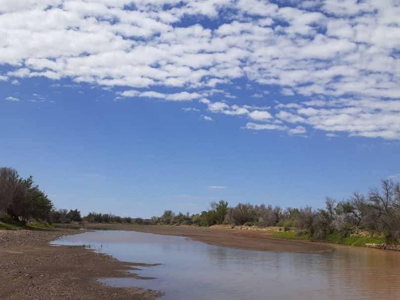 A scenic view of a natural river flowing through the farm landscape under a clear blue sky.