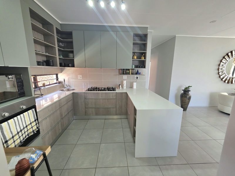 Modern kitchen featuring sleek grey cabinetry, stone countertops, a gas hob, built-in oven, and a functional breakfast bar with tiled flooring.
