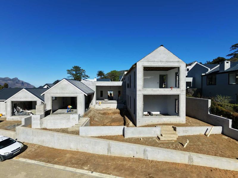 Aerial view of a residential property under construction, featuring a multi-level concrete structure, retaining walls, and an unfinished exterior landscape.